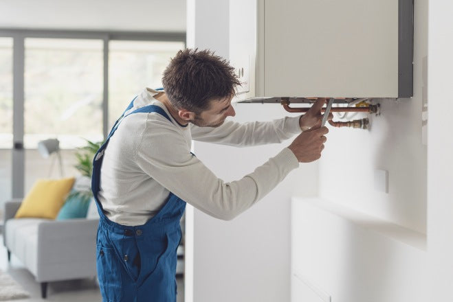 Engineer in blue overalls fixing boiler in a home