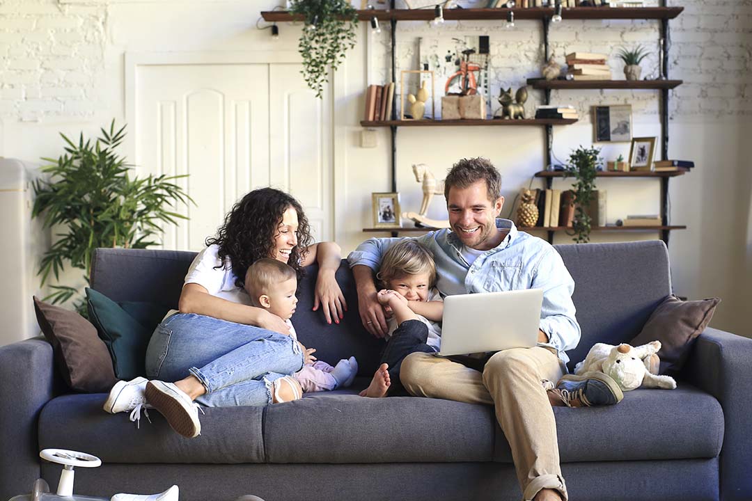 Family of 4 at home on the sofa using laptop