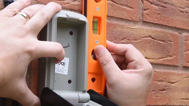 Man using a level to install a Supra C500 Pro key safe on brick wall