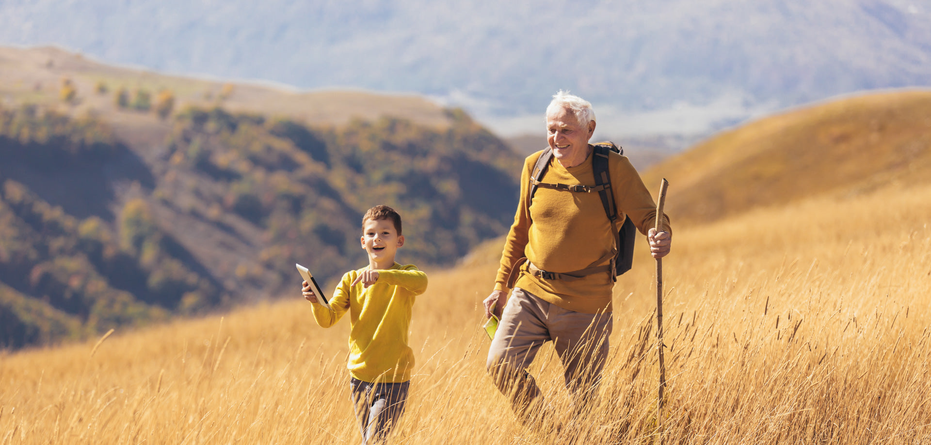 Grandad and grandson walking through wheat field with iPad