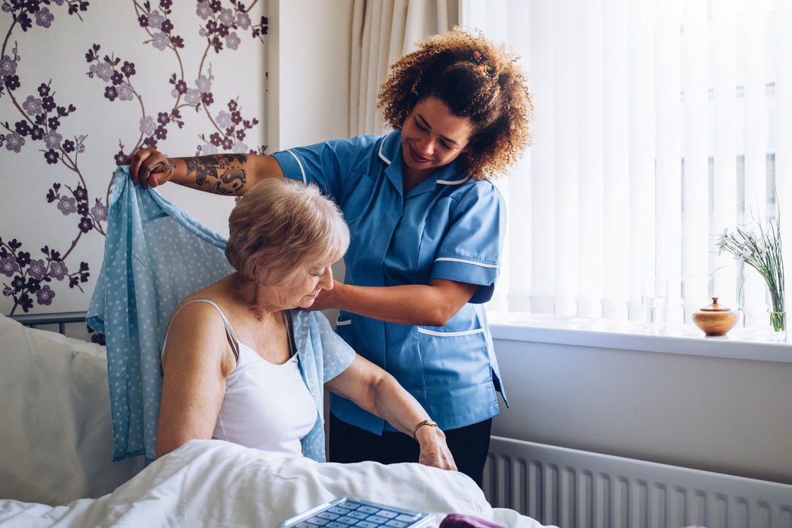 Occupational therapist helping older lady dress whilst in bed