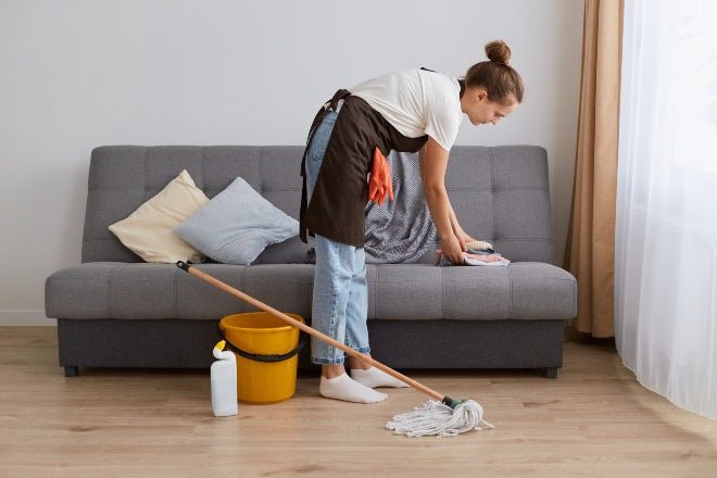 Cleaner tidying up sofa of holiday home with mop and bucket