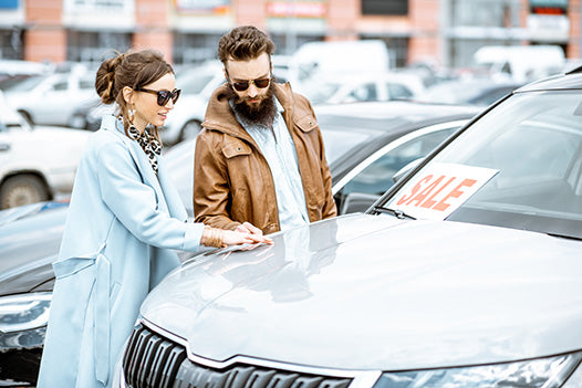 couple looking at a silver car with a for sale sign on it