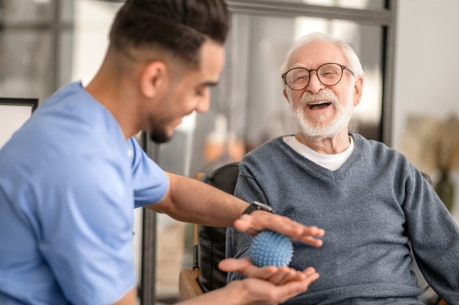 Male occupational therapist using spiky ball on hand of happy man in wheelchair