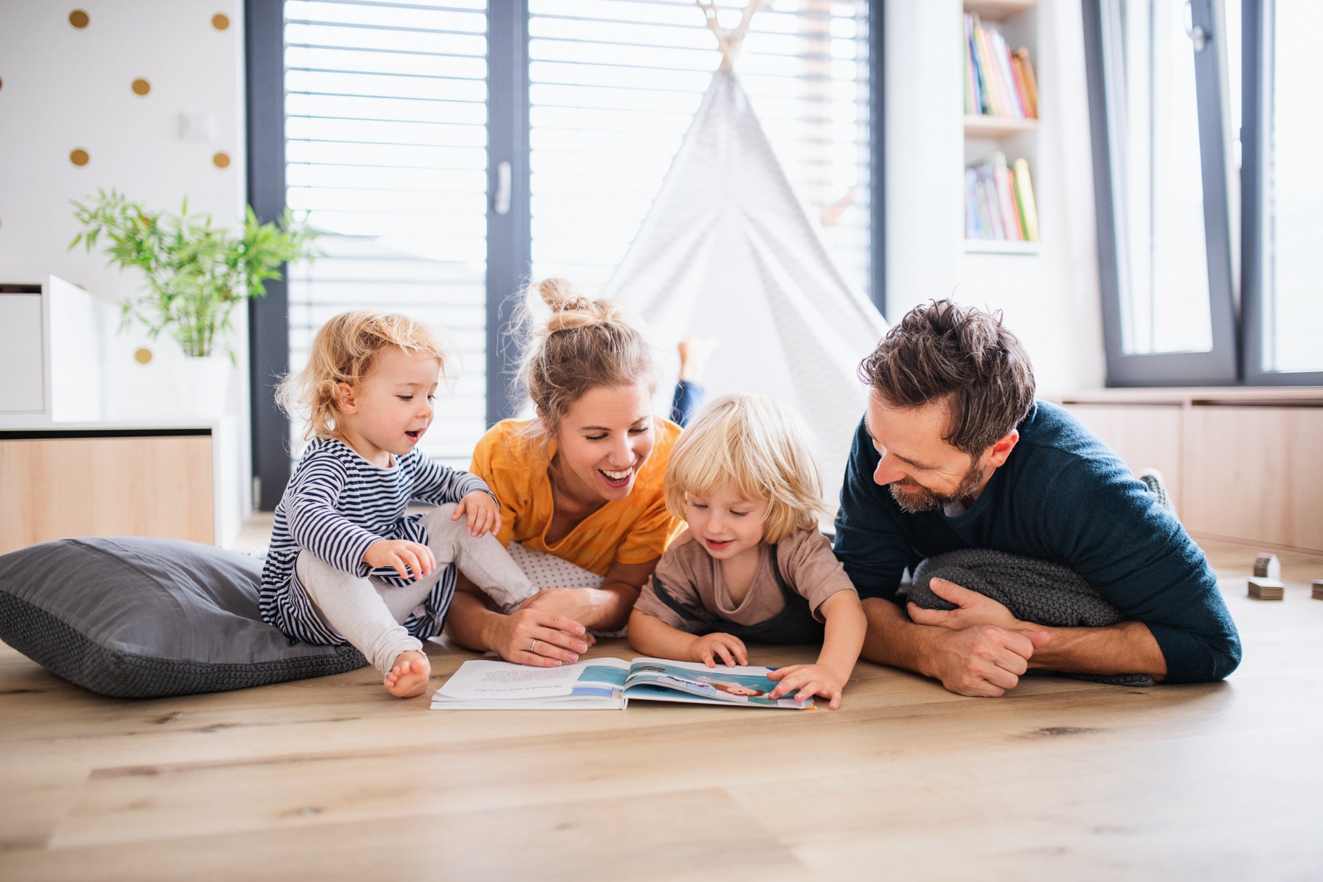 Family with young children reading book on floor of living room