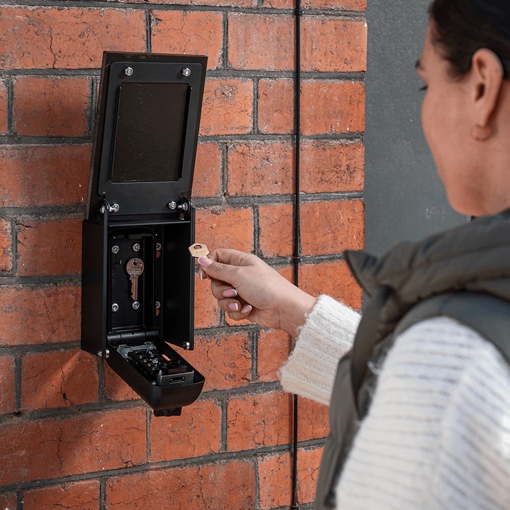 Woman taking key out of key safe hidden behind key safe cover KEYP